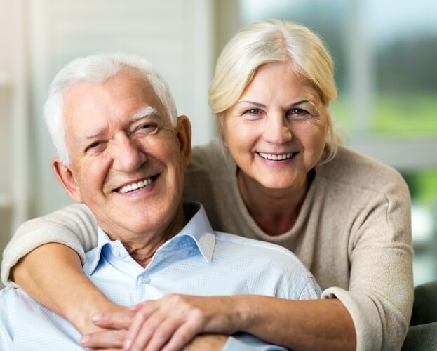 Older man and woman with healthy smiles thanks to maintaining and caring for dental implants