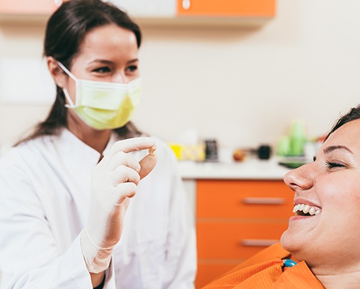Dentist in white coat and yellow mask showing patient extracted tooth