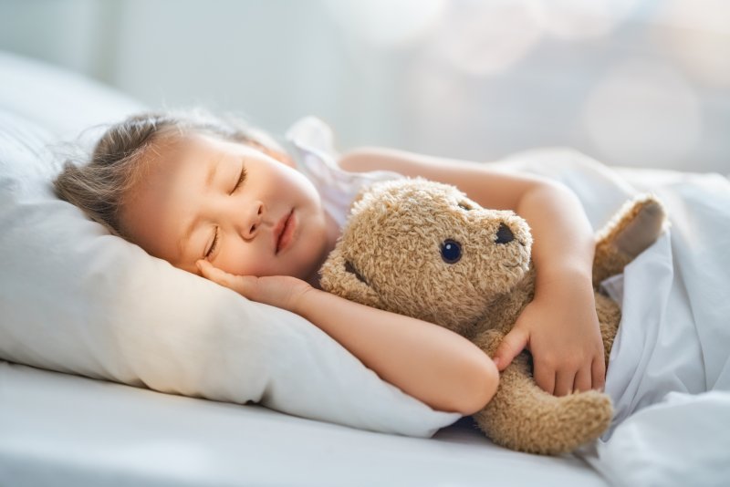 a little girl in bed holding her teddy bear and sleeping