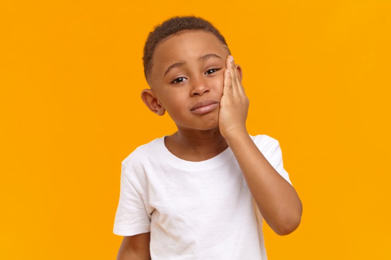 a little boy wearing a white t-shirt and holding his jaw because of increased pain