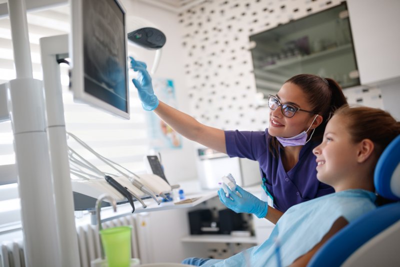 a child looking at their dental X-rays on a nearby monitor while the dentist explains