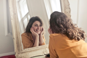 Woman looking in mirror after breaking nail biting habit.
