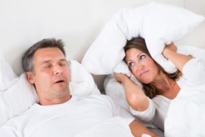 Man snoring with wife covering head with pillow