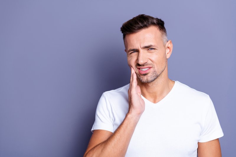 man holding cheek from tooth pain