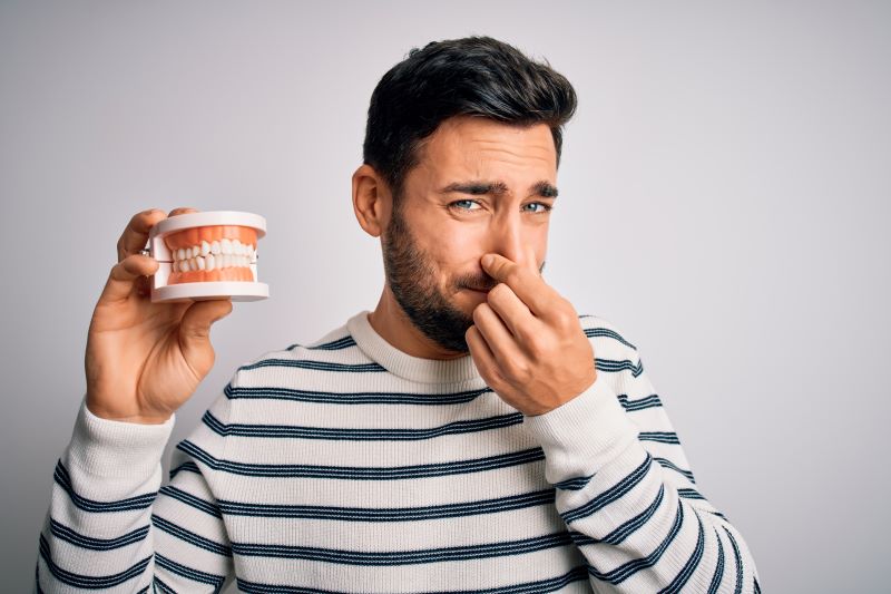 man holding up a set of dentures and holding his nose