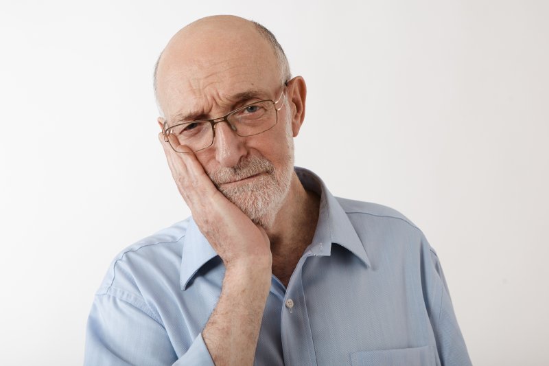 Older man holding his cheek due to ill-fitting dentures