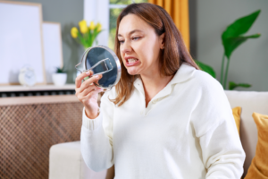 a woman looking at her teeth in a handheld mirror